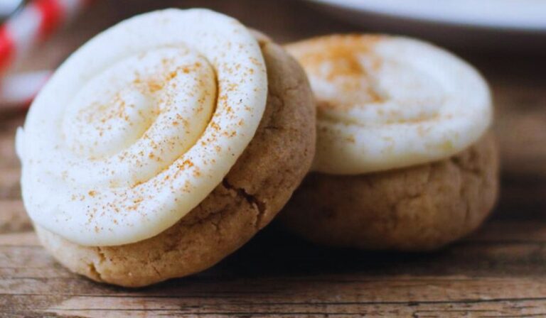 Freshly baked cinnamon roll sugar cookies on a white plate, showcasing a golden-brown texture with a visible swirl of cinnamon and sugar, garnished with a drizzle of creamy icing, perfect for a sweet treat.